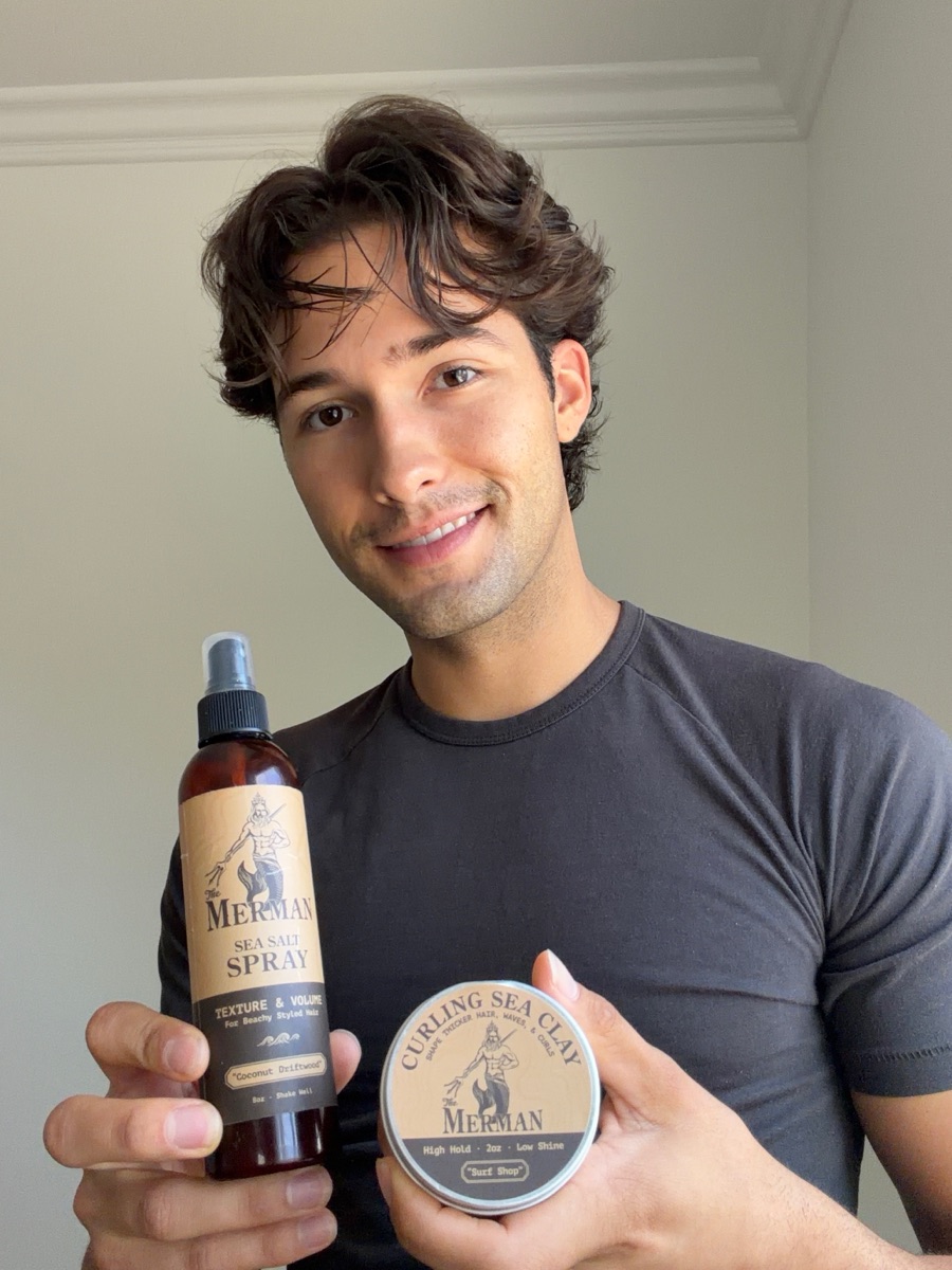 Braiden smiling and holding The Merman sea salt spray and curling sea clay